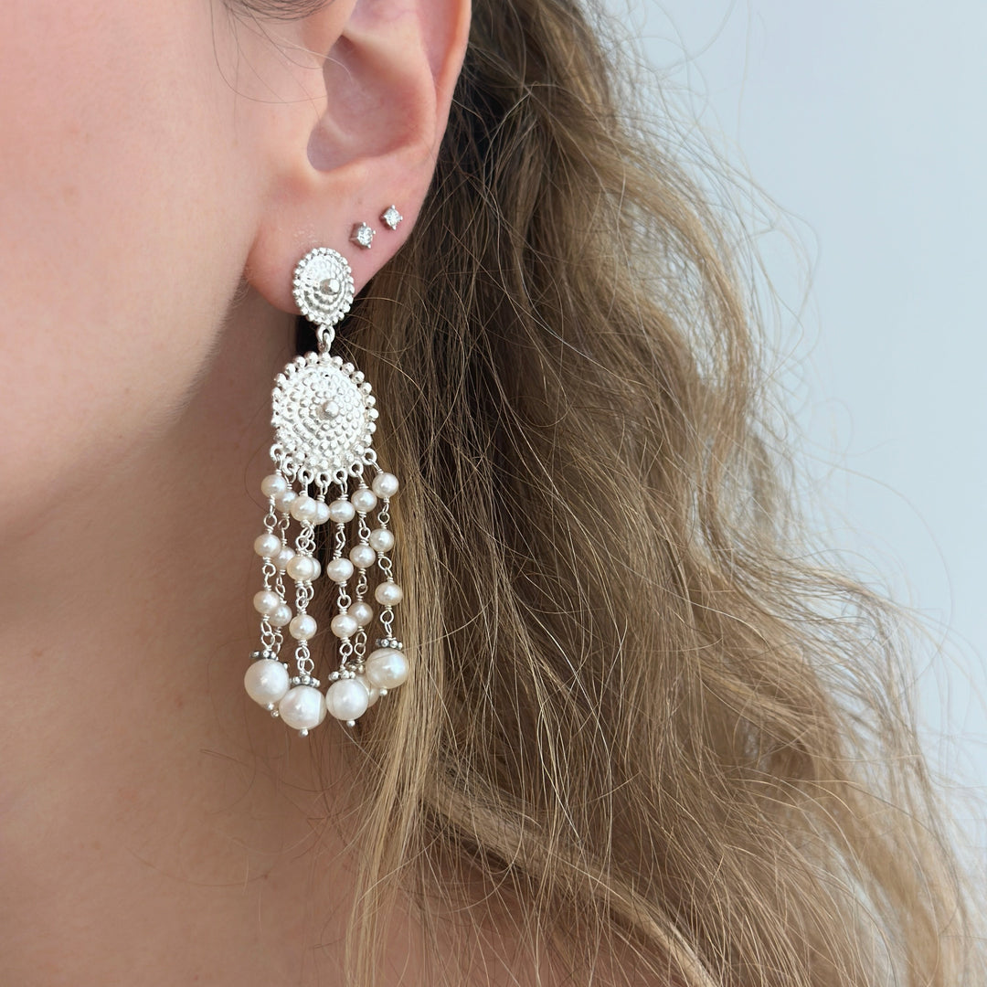 Close-up of a person wearing a silver earring with pearl-like beads against a neutral background