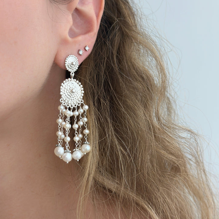 Close-up of a person wearing a silver earring with pearl-like beads against a neutral background